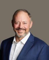 James Tate, Director at JES, smiling, wearing a navy suit jacket and white open-collar shirt