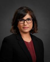 Simmi Sandhu, Director at JES, wearing black-framed glasses, a black blazer and a burgundy top