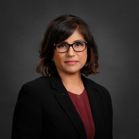 Simmi Sandhu, Director at JES, wearing black-framed glasses, a black blazer and a burgundy top
